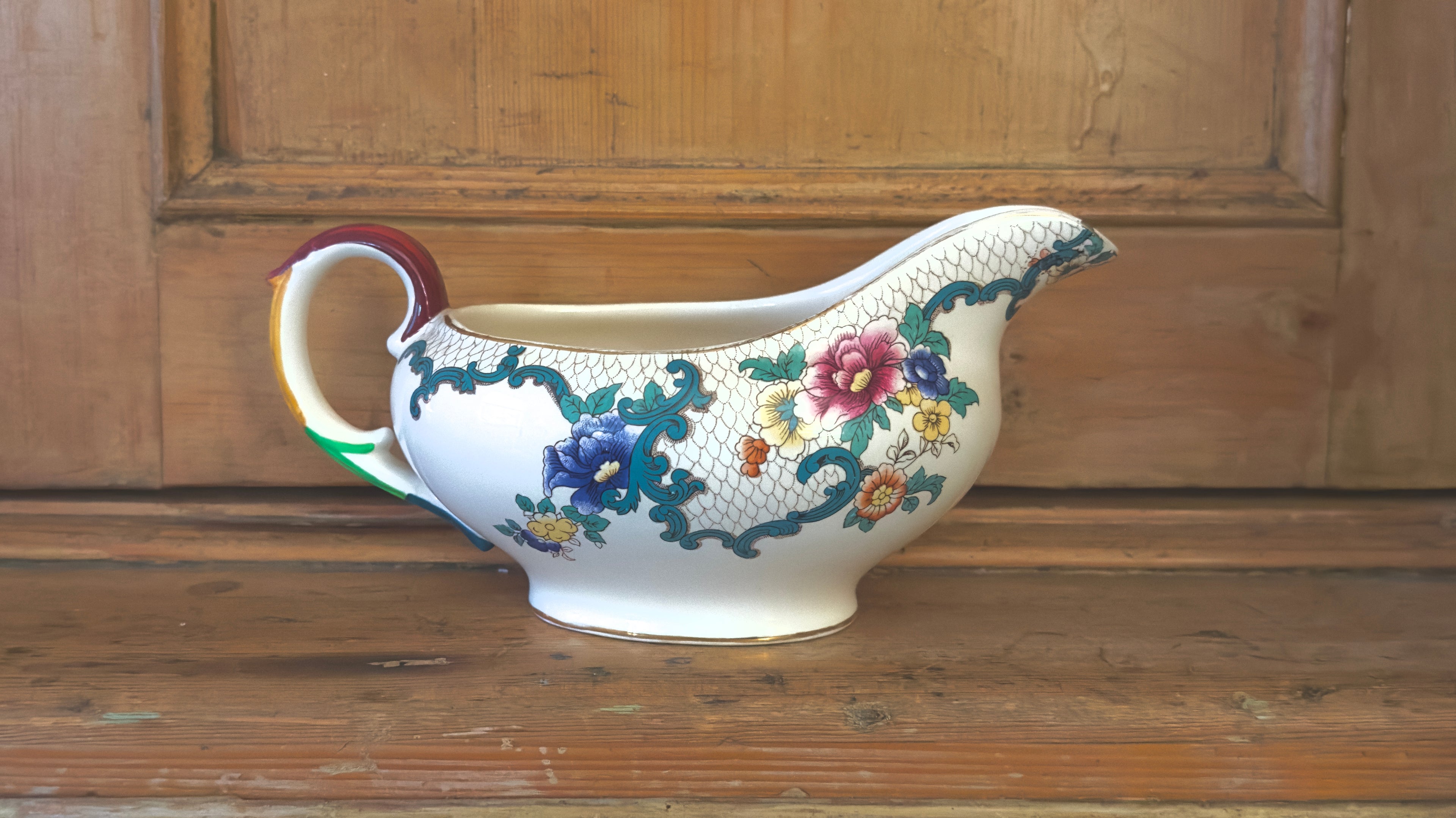 Decorative ceramic gravy boat with floral patterns on a wooden surface